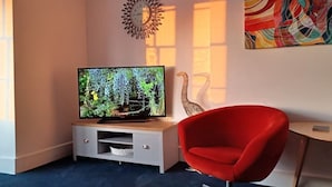 En moderne stue med et fladskærms-tv på et træstel, en rød lænestol og en dekorativ vægdekoration.