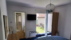 Et soveværelse med en seng, en trækommode, et fjernsyn monteret på væggen, og en dør der fører ud til en balkon med udsigt.