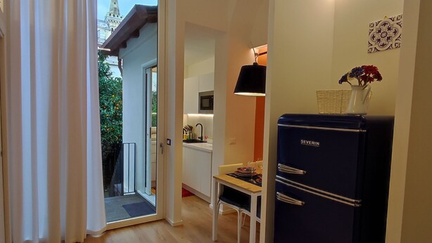 Eine moderne Küche mit weißen Schränken, einer Mikrowelle und einem schwarzen Kühlschrank. Ein Esstisch mit Stühlen und eine Vase mit Blumen stehen auf der Arbeitsplatte.