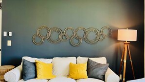 A living room with a dark blue wall, a white sofa with yellow and gray cushions, a wooden coffee table, and a floor lamp. - Appaltree Bungalow: Two bedrooms in town (Boone)