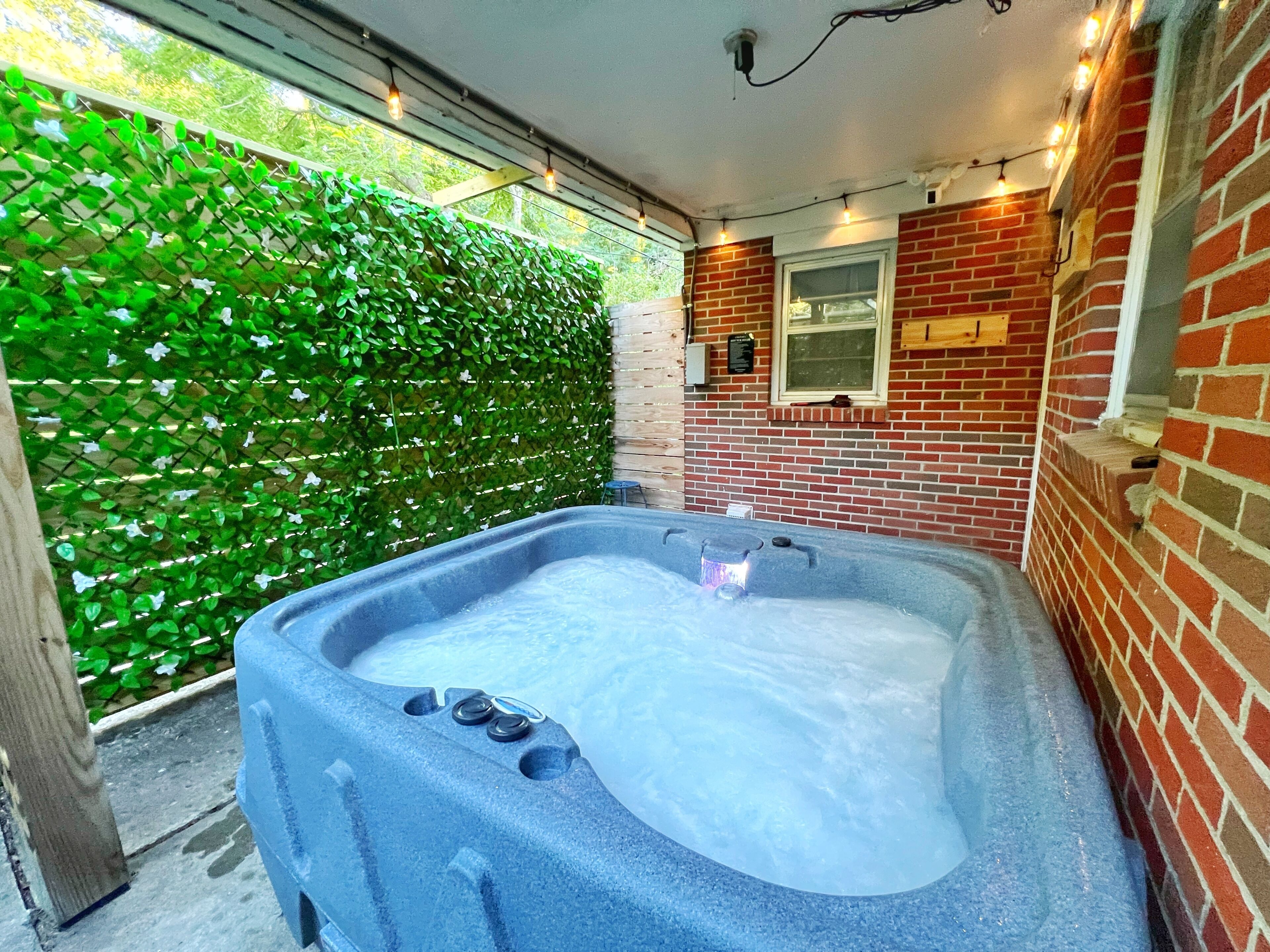 A hot tub with a brick wall and a green hedge in the background.