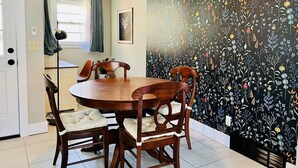 A dining area with a round wooden table and four chairs, a hanging light fixture, and a wall with a floral pattern. - Appaltree Bungalow: Two bedrooms in town (Boone)