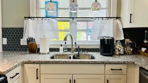 A kitchen with a granite countertop, a stainless steel sink, a coffee maker, and a window with decorative curtains. - Appaltree Bungalow: Two bedrooms in town (Boone)