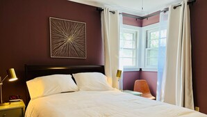 A neatly made bed in a room with a dark wall, a window with white curtains, and a wall-mounted abstract art piece. - Appaltree Bungalow: Two bedrooms in town (Boone)