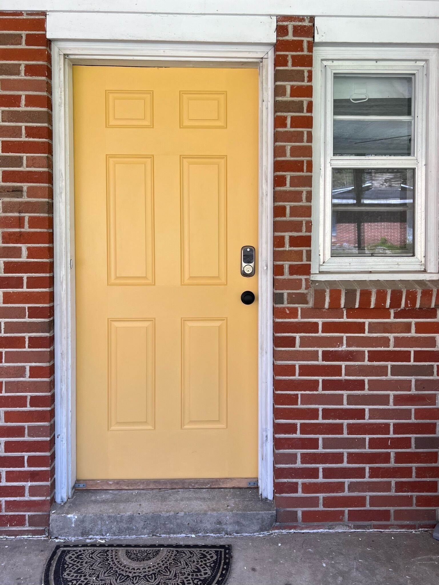 A yellow door with a keypad lock, set in a brick wall with a window above it.