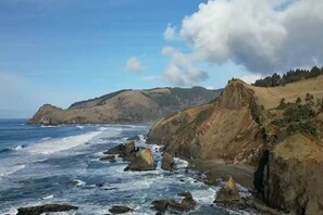 A coastal landscape with rocky cliffs, ocean waves, and distant hills.