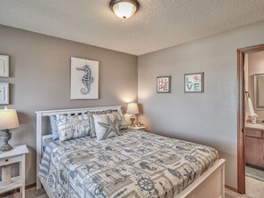 Une chambre à coucher comprenant un lit, des tables de chevet, des œuvres d’art murales et une porte donnant sur une salle de bain.