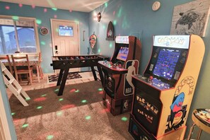 Une pièce avec deux bornes d’arcade, une table de baby-foot et une porte avec une fenêtre.