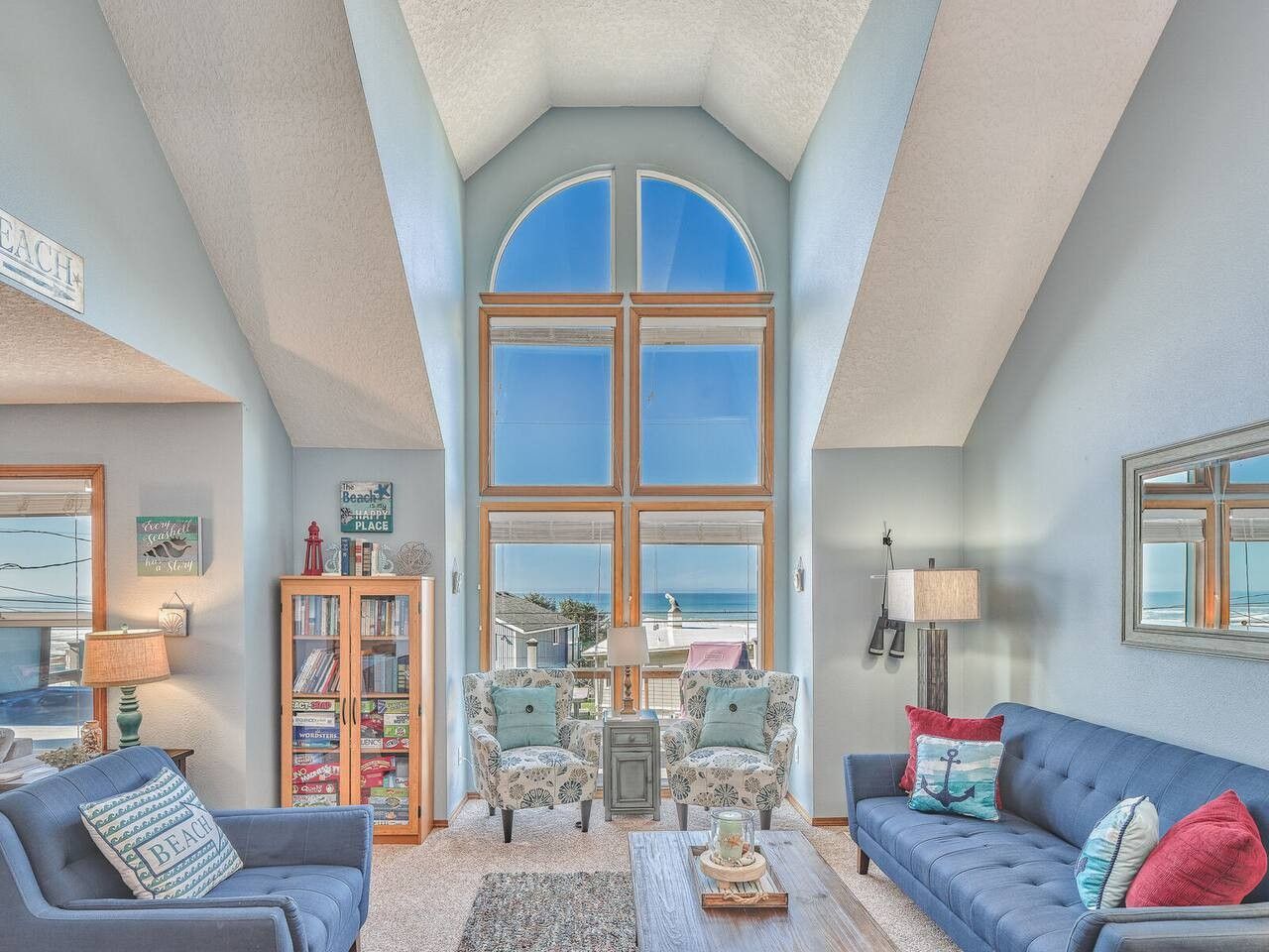 A spacious living room with a high ceiling, large windows, and a view of the sea.