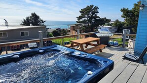 Un jacuzzi en una terraza con vista al océano, una parrilla de barbacoa y una mesa de picnic.