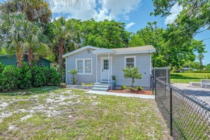 A single-story house with a front porch, surrounded by a chain-link fence, and a small yard with sparse grass and a few trees. - Pet-Friendly Cottage Near Beach: King Bed/Fire Pit (Bonita Springs)