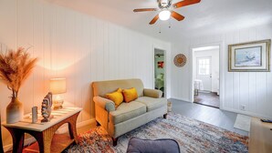 Ein Wohnzimmer mit Deckenventilator, einer Couch mit Kissen, einem Tisch mit Lampe und einem Teppich.