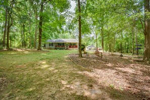 A house surrounded by a wooded area with a lawn and a small deck.