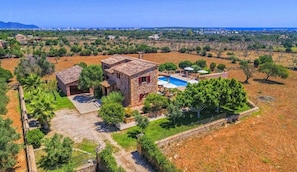 A stone villa with a swimming pool, surrounded by a landscaped garden and a view of the sea.