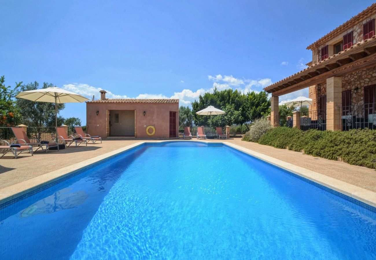 Ein Swimmingpool mit Liegestühlen und Sonnenschirmen, umgeben von Gebäuden mit Steinmauern und roten Fensterläden.
