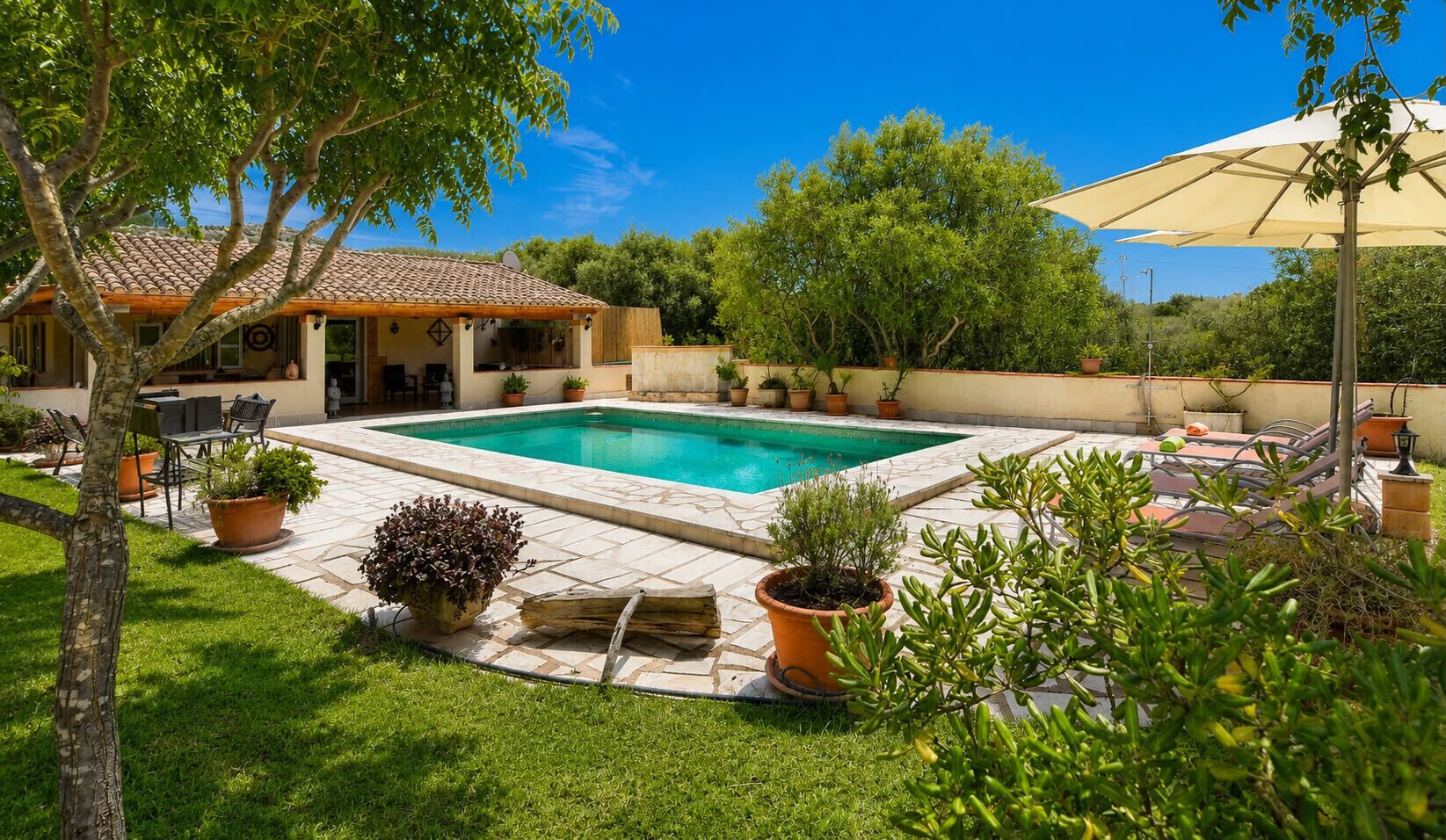 A swimming pool with a tiled deck, surrounded by potted plants and outdoor furniture.