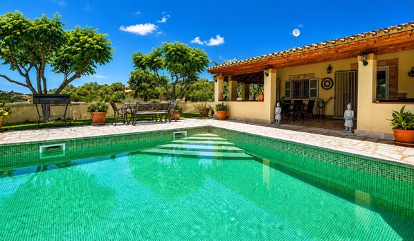 A swimming pool with a tiled edge, surrounded by potted plants and outdoor furniture.