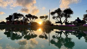 A serene outdoor pool area with lounge chairs and umbrellas, surrounded by trees, reflecting the sunset and sky. - 3 bedroom country house with private pool and barbecue (Son Macià)