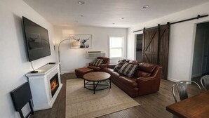 Een moderne woonkamer met een open haard, een leren bank en een televisie aan de muur.