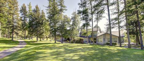 A well-maintained lawn with a pathway leading to a house surrounded by tall trees.