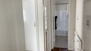 Un pasillo con una puerta blanca, un baño con bañera y un armario blanco.