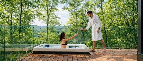 A wooden deck with a hot tub, surrounded by trees and a clear sky.