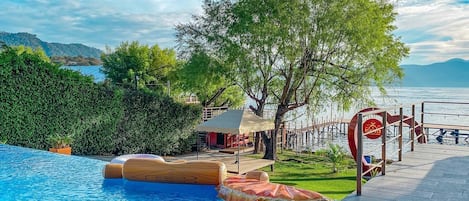 A pool area with a wooden deck, a covered seating area, and a view of the water.