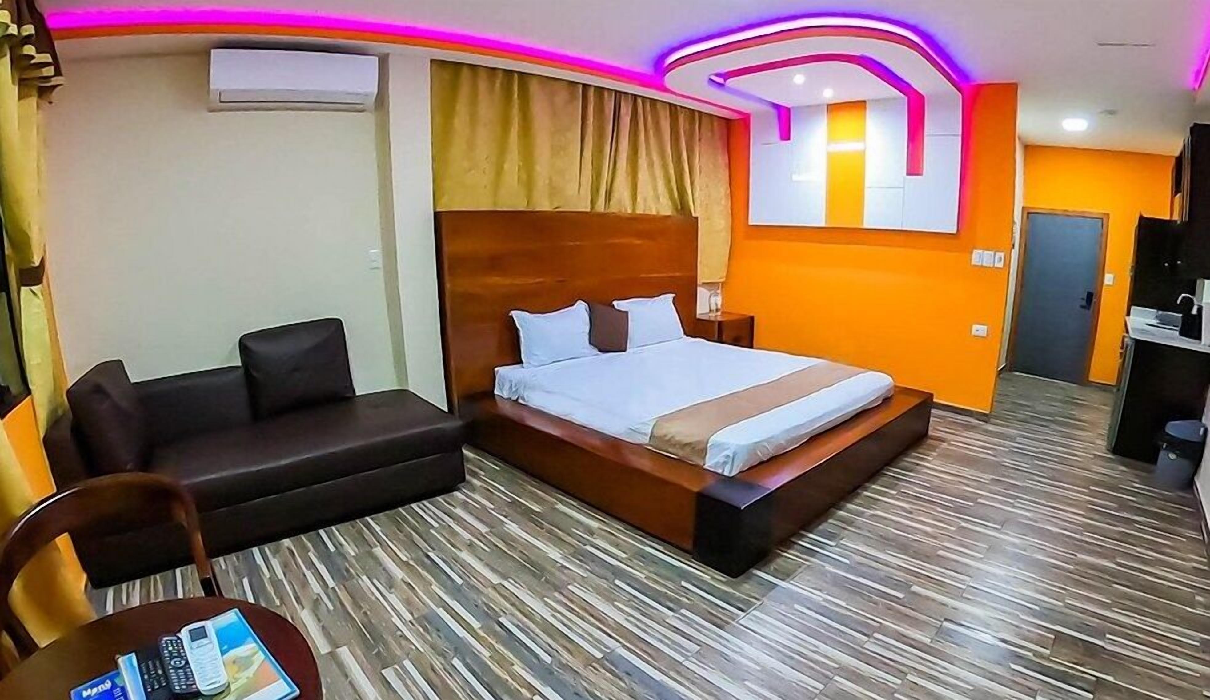 A hotel room with a bed, a sofa, a small table with a chair, and a TV.