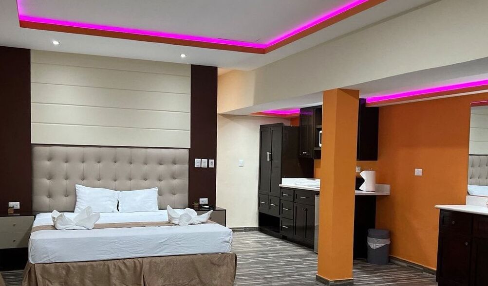 A modern hotel room with a large bed, a bathroom with a sink, and a mirror.