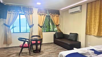 A hotel room with a bed, a sofa, a dining table with chairs, and a window with curtains.