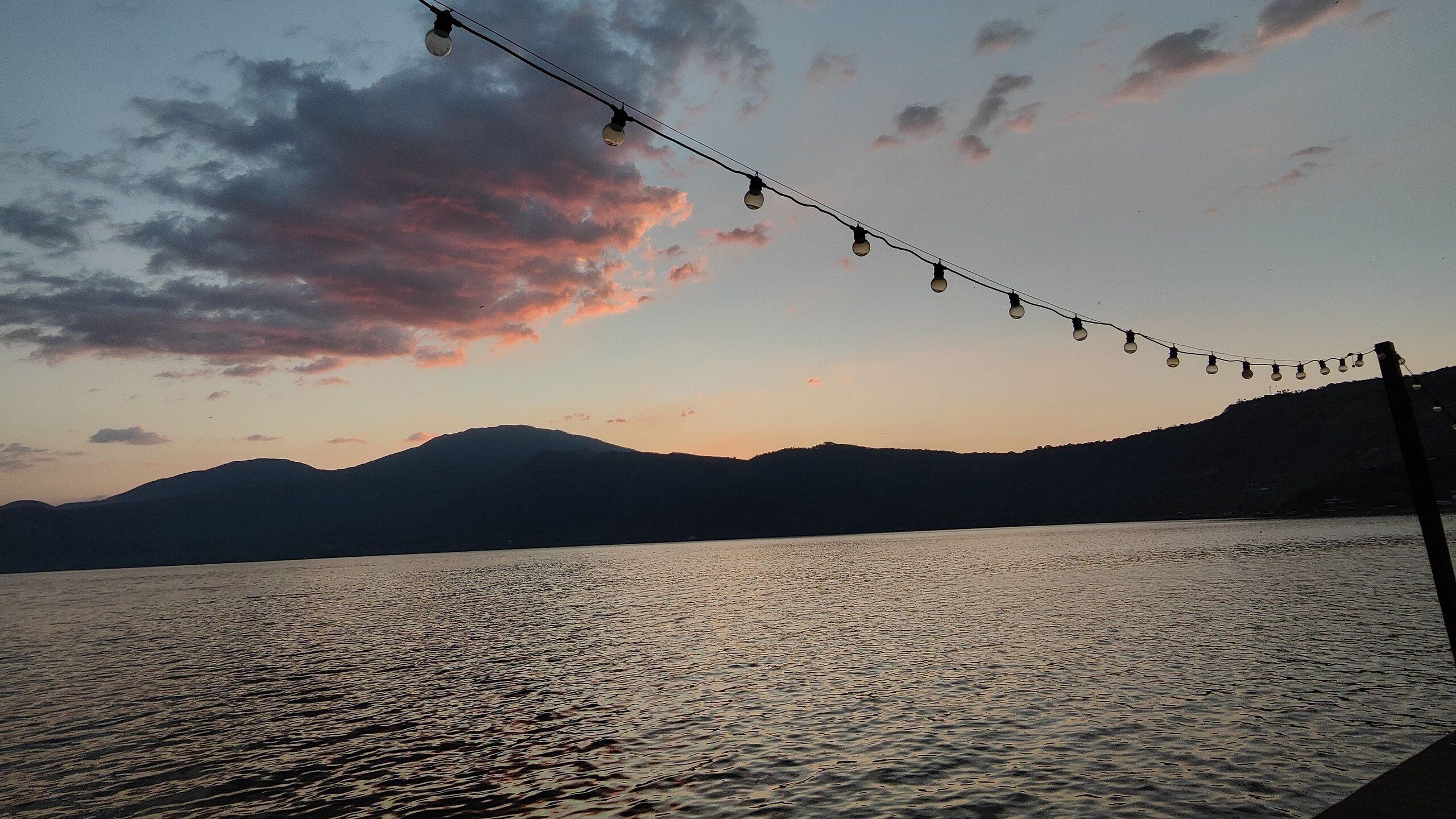 A sunset over a body of water with mountains in the background and string lights overhead.