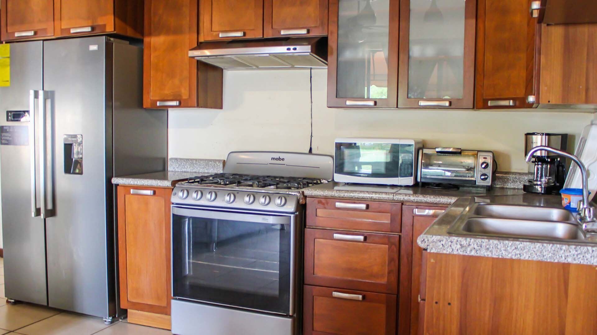 Una cucina con mobili in legno, un frigorifero in acciaio inossidabile, un fornello, un forno a microonde, un tostapane e una macchina per il caffè.