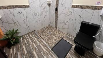 A bathroom with a shower area, a toilet, and a small rug.