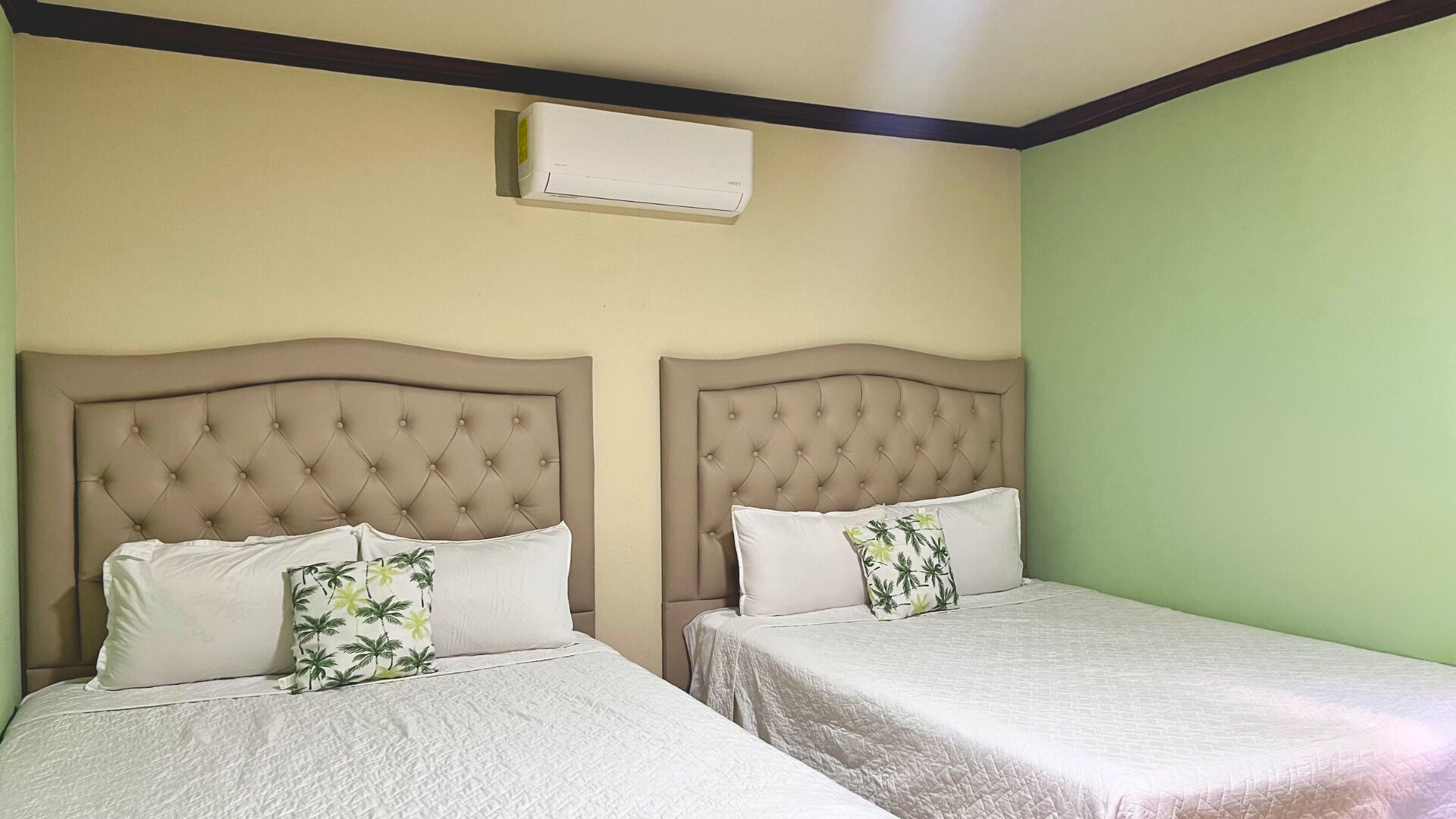 Two beds with tufted headboards, a wall-mounted air conditioner, and a green wall.