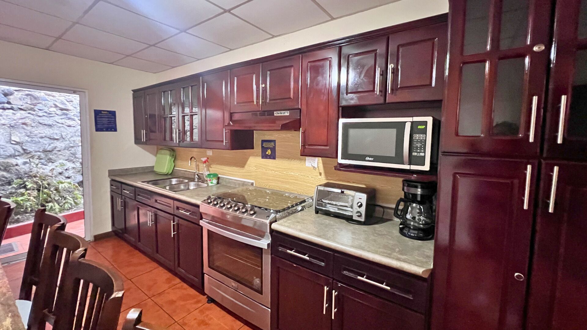 A kitchen with dark wooden cabinets, a stainless steel sink, a microwave, a toaster, and a coffee maker.