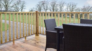 Eine Holzterrasse mit Tisch und Stühlen mit Blick auf ein Wiesenfeld.