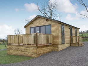 Une cabane en bois dotée d’une terrasse, de grandes fenêtres et d’une cheminée.