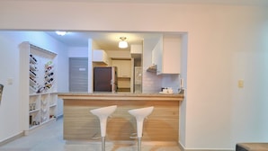 A modern kitchen with a wooden countertop, two white bar stools, and a built-in shelving unit with shoes.