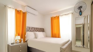 A bedroom with a bed, nightstand, lamp, and a wall-mounted fan.