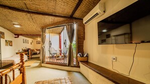 A room with a wooden bed, a woven mat, a dining area with a table and chairs, and a large window with curtains. - Ferraria Guest House (Paraty)