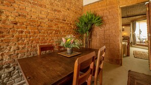 A dining area with a brick wall, wooden table, chairs, and a potted plant with flowers. - Ferraria Guest House (Paraty)