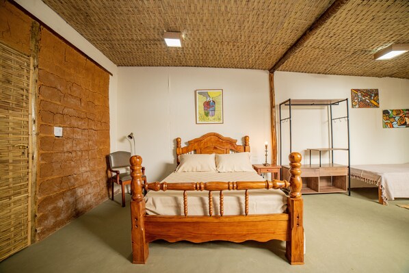 Una habitación con una cama de madera, una silla, una mesita y una pared con un cuadro.