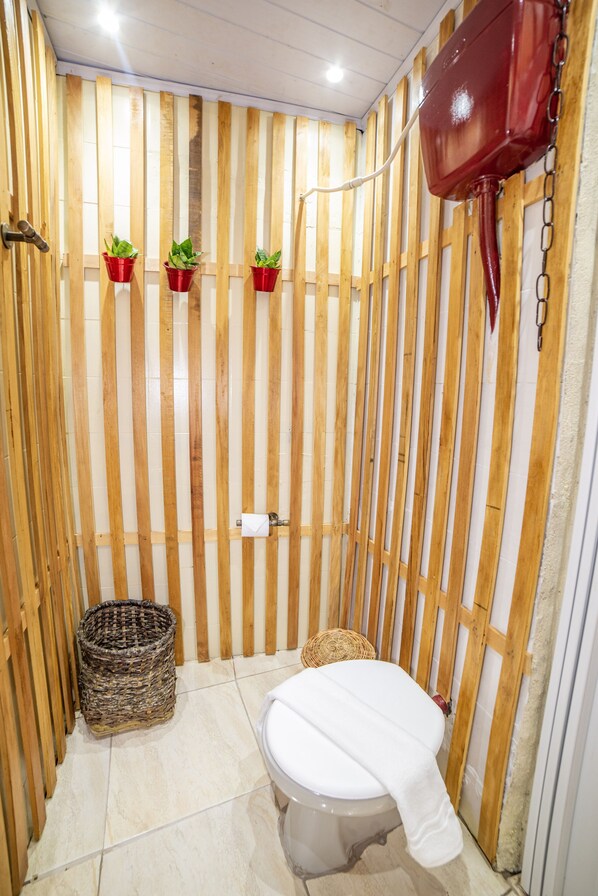 A small, narrow bathroom with wooden slats, a toilet, a red toilet tank, and three potted plants.