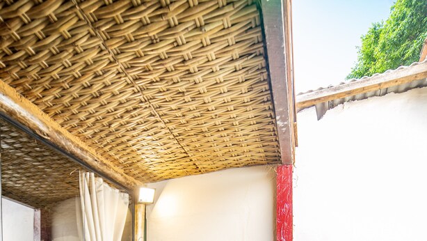A wooden deck with a woven ceiling, a metal chair with a cushion, and a wooden table with a bottle and a flower. - Ferraria Guest House (Paraty)
