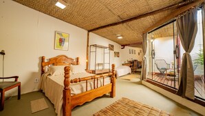 A room with a wooden bed, a bench, a large window with curtains, and a view of the outdoors. - Ferraria Guest House (Paraty)
