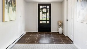 A hallway with a black door, white walls, and a tiled floor. - Lake Ontario Beauty! Sleeps 4! (Williamson)