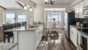A kitchen with granite countertops, white cabinetry, a dining area with a table and chairs, and a view to the outside. - Lake Ontario Beauty! Sleeps 4! (Williamson)