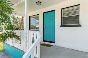 Een huis met een blauwgroene deur, een veranda met een witte leuning en een raam met luiken.
