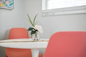 A round white table with a clear glass vase containing white flowers and green leaves, set on a white tablecloth.