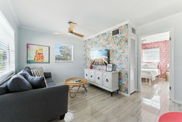 A living room with a grey sofa, a round wicker table, a white cabinet with floral wallpaper, and a ceiling fan.